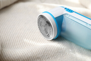 Modern fabric shaver on beige woolen sweater, closeup. Space for text