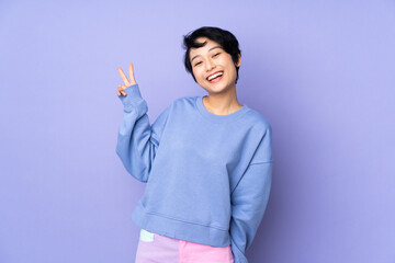 Young Vietnamese woman with short hair over isolated purple background smiling and showing victory sign