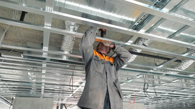 A construction worker assembles metal suspended ceiling structures. Construction and belts in the house