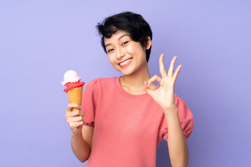 Young Vietnamese woman with short hair holding a cornet ice cream over isolated purple background showing ok sign with fingers