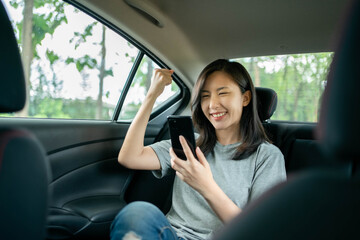 Asian woman sitting in a car is delighted after seeing a message on her cell phone.