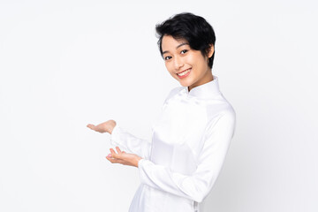Young Vietnamese woman with short hair wearing a traditional dress over isolated white background extending hands to the side for inviting to come