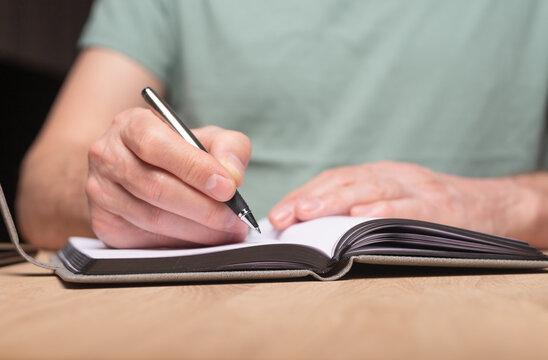 Male hands taking notes, writing plans in notebook or planner. Planning in schedule diary, close up.