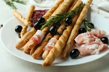 Plate with grissini and snacks on white textured background