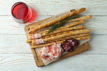 Grissini sticks with bacon and wine on white wooden background