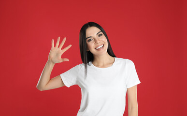 Woman showing number five with her hand on red background