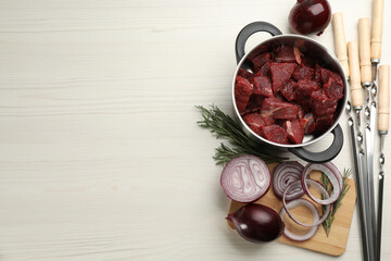 Composition with metal skewers and fresh meat on white wooden table, flat lay. Space for text