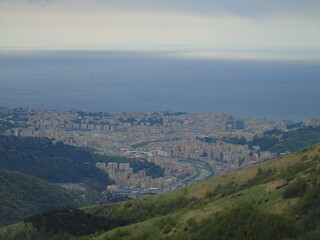 Genova, Italy - April 14, 2021: Panoramic view to the mountains over the city of Genova, and small part of the port. Grey sky in the background.