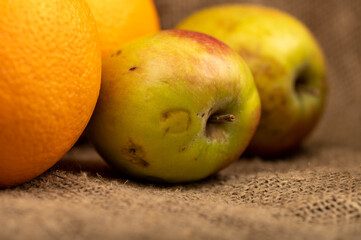 Fresh green apples and juicy oranges on a homespun fabric with a rough texture.