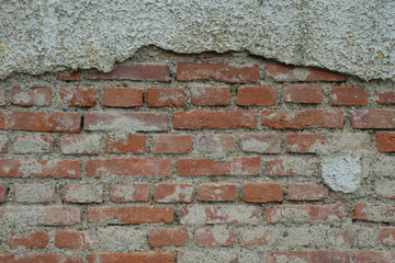 Eine schmutzige alte Mauer / Ziegelmauer aus roten Ziegelsteinen(Textur / Hintergrund / Deko), oben hängen die Reste vom Putz, unten ist der Putz abgebrochen