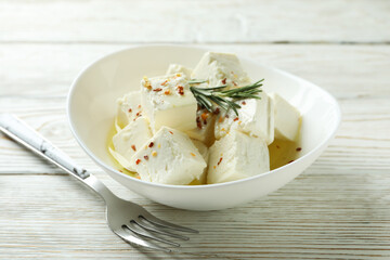 Bowl with feta cheese and fork on white wooden background