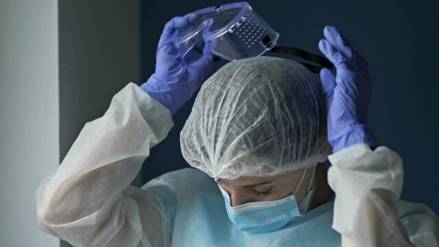 Portrait Of A Tired Female Doctor Or Nurse. The Woman Takes Off Her Goggles And Mask And Breathes A Sigh Of Relief. Pandemic Covid-19.