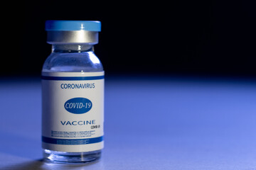 Coronavirus vaccine. Pandemic banner. Covid-19 inoculation. Healthcare industry. Blue dose vial glass bottle with label on defocused dark copy space background.