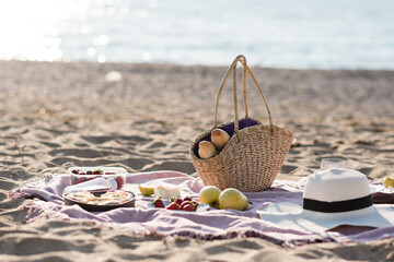 Having picnic with fresh bread, straw bag and hat on blanket at sandy beach over sea shore at...
