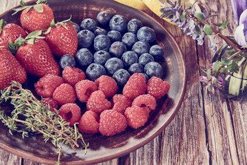 Ripe berries on a ceramic plate on a wooden background.