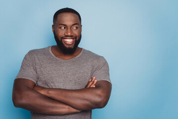 Positive dark skin guy hold arms crossed look empty space isolated blue background