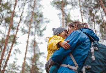 Fototapeta na wymiar Happy family Mom and child walk in the forest after rain in raincoats together, hug and look at each other