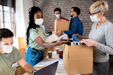 Group of volunteers with face mask working in community charity donation center.