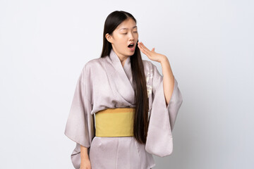 Fototapeta premium Young Chinese girl wearing kimono over isolated background yawning and covering wide open mouth with hand