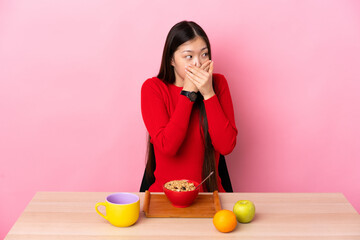 Young Chinese girl  having breakfast in a table covering mouth and looking to the side