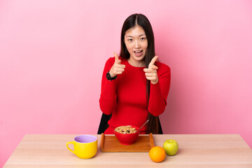 Young Chinese girl  having breakfast in a table pointing to the front and smiling
