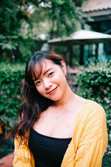 Close up of young pretty Asian woman in blue yellow sweater with garden background.