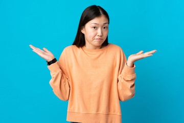 Young Chinese girl over isolated blue background having doubts while raising hands