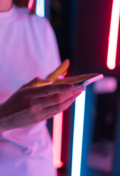 Phone in the hands of a young woman close up in the light of neon