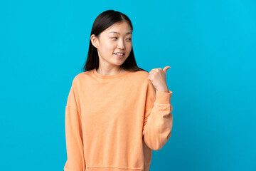 Young Chinese girl over isolated blue background pointing to the side to present a product