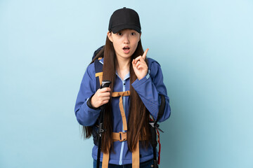 Young Chinese girl with backpack and trekking poles over isolated blue background intending to realizes the solution while lifting a finger up