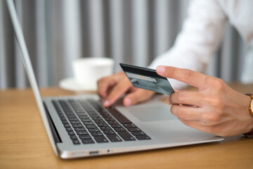 Young man hand holding credit card on office deck with laptop, coffee to pay for items through an online payment system. Online shopping is the best option to reduce the spread of the coronavirus.
