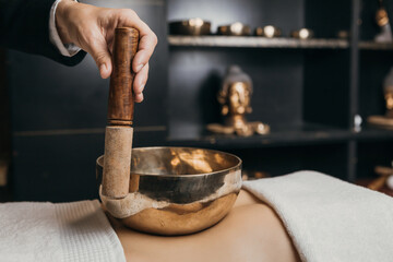 Tibetan singing bowls on the belly and hand. Sound massage with singing bowls on the body. Vibrational therapy. Woman doing relaxing massage, meditation. Stress relief. Spa with Buddha decoration.