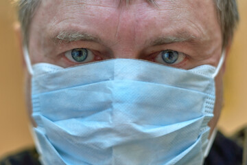 Facial portrait of an adult male wearing a medical mask looking into the camera.