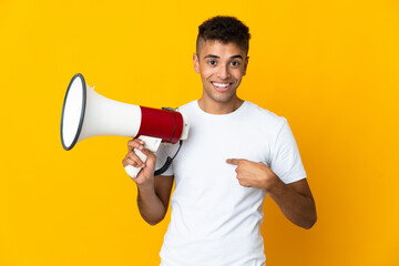 Young brazilian man isolated on yellow background holding a megaphone and with surprise facial expression