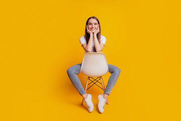 Photo of pretty shiny lady sit chair hands cheekbones wear white t-shirt posing on yellow background