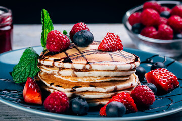 closeup of plate of pancakes with caramel syrup, fresh fruits and mint leaves. small jar of jam background. selective focus