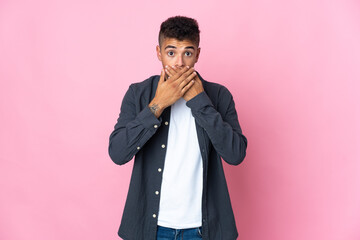 Young Brazilian man isolated on pink background covering mouth with hands