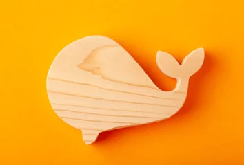 Selbstklebende Fototapeten A figurine of a whale carved from solid pine with a hand jigsaw. On a yellow background © strannik_fox