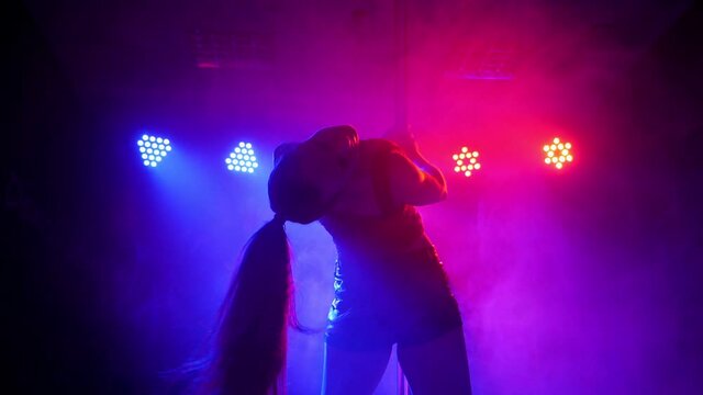 A flexible dancer dances on a pole under the light of colorful spotlights.