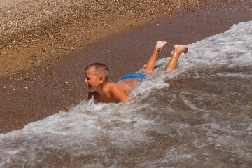 Tanned short-haired nine-year-old boy swims by the sea and plays with the waves in the summer