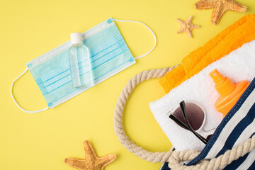 Top view photo of beach bag with towels sunglasses sunscreen orange bottle sanitizer on medical facemask and starfishes on isolated yellow background with copyspace