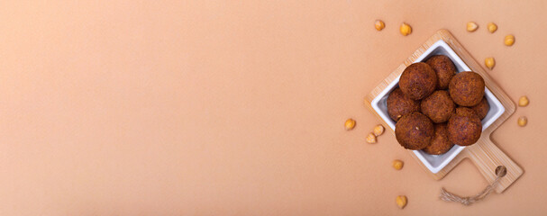 Horizontal banner with fried falafel in square bowl and chickpea on beige background. Healthy roasted vegetarian fastfood. Jewish cuisine. Copy space.