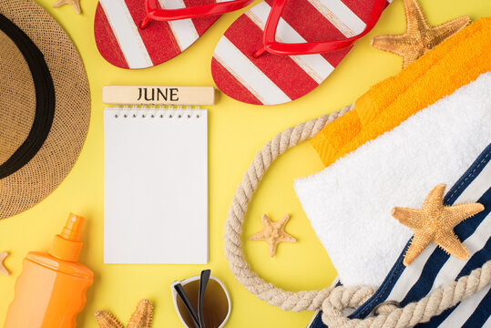 Top view photo of copybook with inscription june starfishes beach bag with orange and white towels sunscreen bottle cap sunglasses and flip-flops on isolated yellow background with blank space