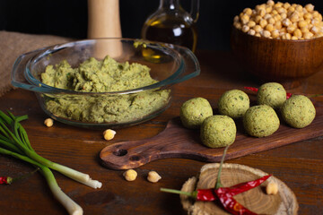 Raw falafel on brown wooden board. Healthy vegetarian food, fitness eating. Falafel indredients on rustic kitchen. Jewish cuisine. Chickpea in bowl, red chili pepper, green onions, olive oil