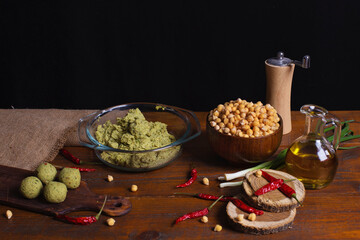 Raw jewish falafel in rustic kitchen on brown wooden board with copy space. Healthy vegan food, fitness eating. Falafel indredients. Chickpea in bowl, red chili pepper, green onions, olive oil