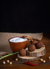 Vertical image with fried falafel on wooden circles and white yogurt sauce in clay bowl on brown board with burlap cloth. Roasted vegetarian food. Jewish cuisine. Green onion and chickpea. Copy space