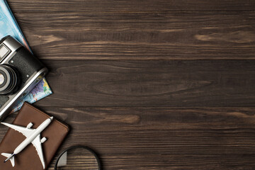 Top view photo of plane model on passport cover magnifier camera and map on isolated wooden table background with copyspace on the right