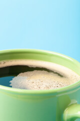 Hot fresh coffee with foam in the green cup on a color background