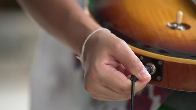 Guitarist connecting electric guitar. Plugging a jack into electric guitar .Close up of 
female hand plugging audio cable in electric guitar 