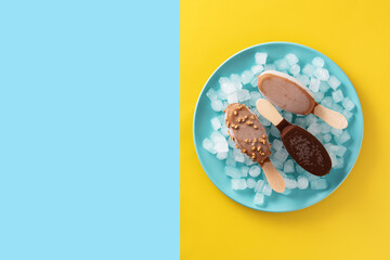 Chocolate popsicles and crushed ice on blue plate on yellow and blue background